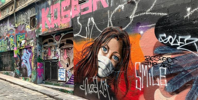 A graffitti painted on a wall, showing a youg woman wearing a face mask and the word SMILE, taken from the Australia Locked Down project.