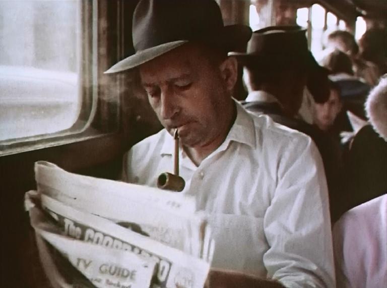 Man, wearing a hat, smokes a pipe and reads the newspaper, on board a Brisbane tram, 1964.