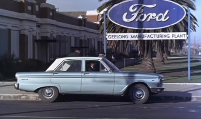A blue car, in front of a sign reading 'Ford Geelong Manufacturing Plant'