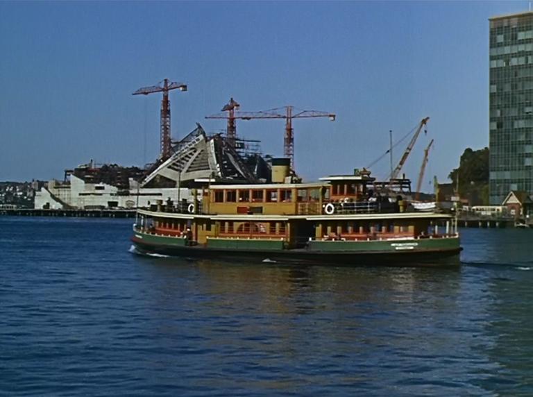 Sydney Harbour and Circular Quay, with a ferry passing in front of the Sydney Opera House, still under construction