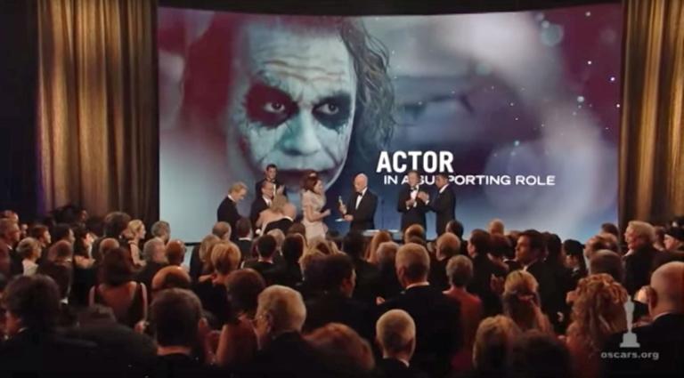 A large screen shows an image of Heath Ledger as The Joker in The Dark Knight. In the foreground Ledger's family go up on stage at the Oscars to accept the award on his behalf.