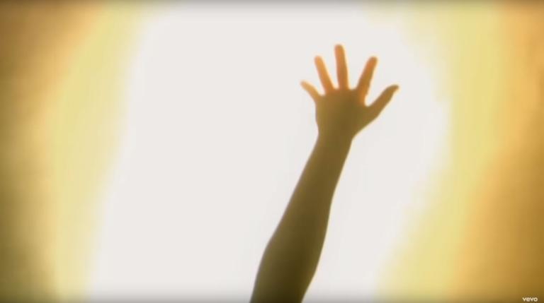 An arm and hand is being held up sillouhetted by bright light.