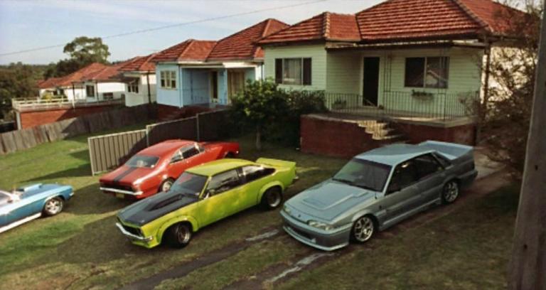 Four cars sit in the driveway of an Australian suburban house.