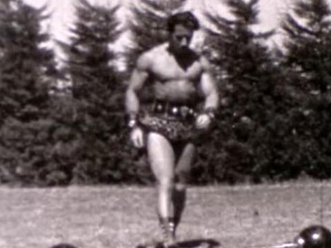 A strongman wearing a loin cloth approaches a barbell