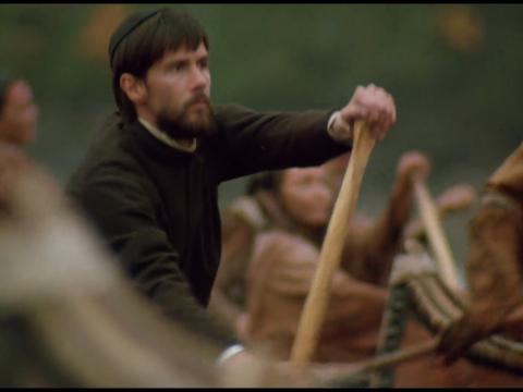 A man dressed in priest's clothing paddling a canoe.