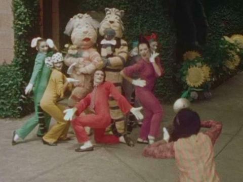 Still from a behind the scenes film about Hector the Cat showing characters Hector and Milly exiting a church like a married couple as people in coloured cat costumes dance around them.