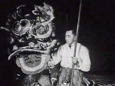 A Chinese man holding a pole standing beside a large dragon head during a dragon dance at Chinese New Year celebrations