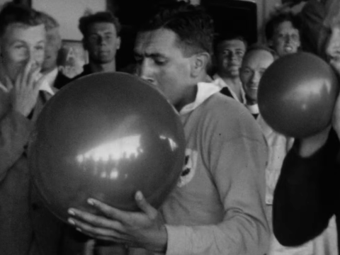 a couple of men blow up balloons while others watch