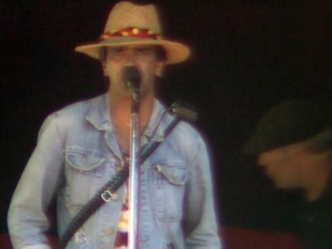 A man wearing a hat and a denim jacket standing in front of a microphone.
