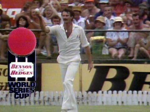 Cricketer Dennis Lillee on a cricket oval holding up a cricket ball with one hand with spectators cheering in the background. Next to him is a graphic overlay of a logo for the Benson and Hedges World Series Cup.