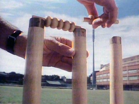 Close up of a person's hands placing a bail onto some cricket stumps