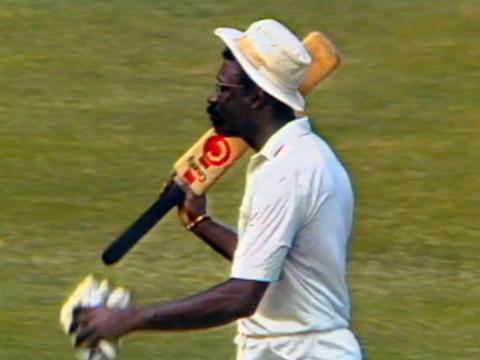 West Indian cricket player Clive Lloyd pictured from the waist up. He is walking on a cricket oval holding a cricket bat.