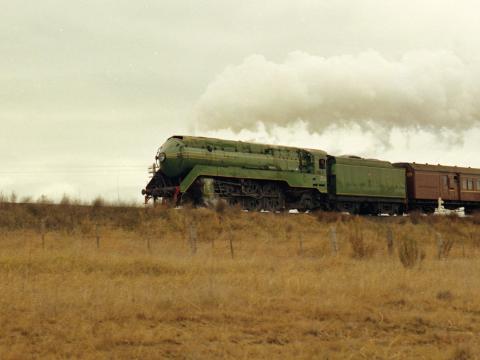 A 3801 steam locomotive pulling a passenger train through the countryside.