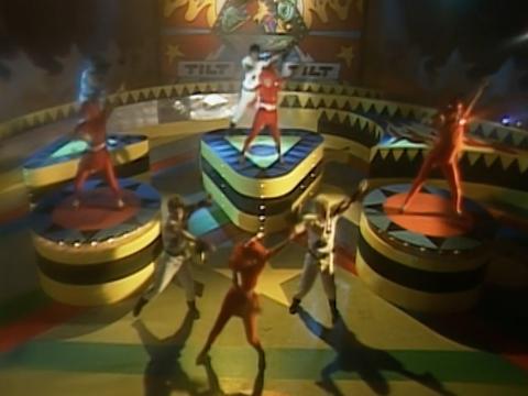children in bright costumes dance on a stage that looks like an oversized pinball machine