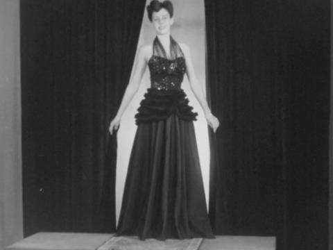 A female model in formal evening wear on the runway at a 1940s fashion show.
