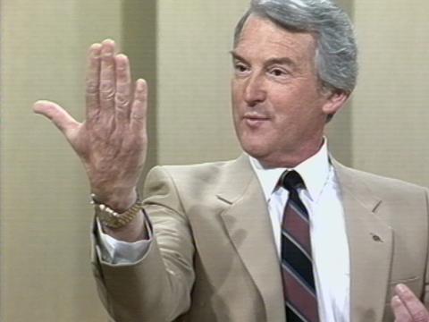 Roger Climpson OAM with his hand raised, mid-sentence telling a story. 