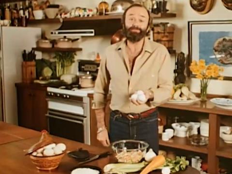 Peter Russell-Clarke in his kitchen, holding 3 eggs in his right hand while speaking to the camera