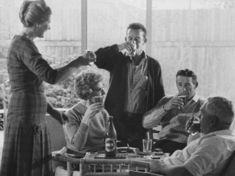 Black-and-white image of a family around a table, with the men drinking VB.