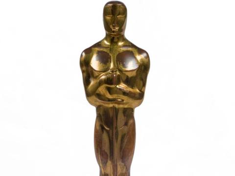 A gold Academy Award statue seen from the waist up, with a man clutching the handle of a sword