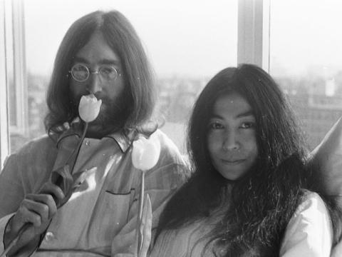 John Lennon is sniffing a tulip. Yoko Ono holds a tulip and looks at the camera.