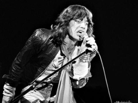 A black and white image of Mick Jagger singing into a microphone.