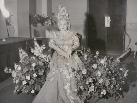 Marjorie Lawrence wearing an elaborate dress and surrounded by floral displays.