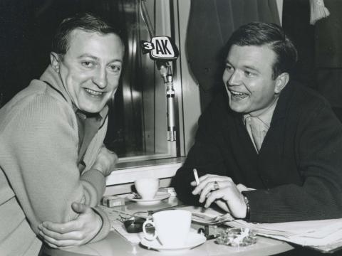 Graham Kennedy smiling to camera sitting opposite Bert Newton in front of a 3AK microphone