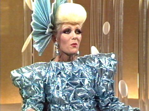 Jeanne Little wearing a blue metalic dress and a fan-like hat.