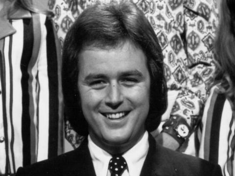 Black and white still of Johnny Young, smiling. He is wearing a shirt and tie.
