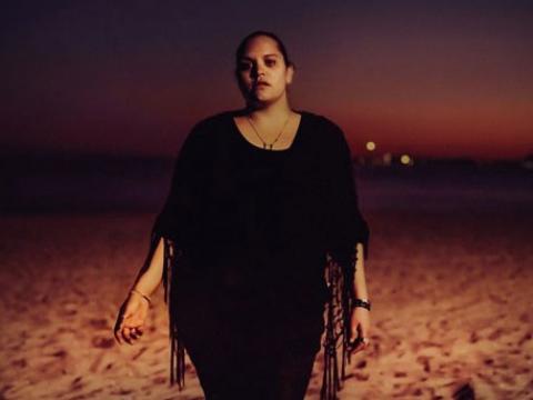 Indigenous woman walking towards the camera at night on a sandy beach.