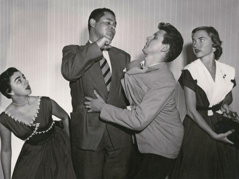 A man aiming to punch another man while two woman look on
