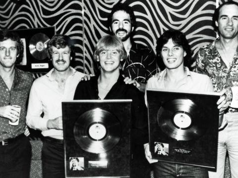 John Farnham and his band members in 1980 holding his gold record for 'Uncovered' and smiling at camera.