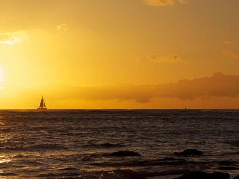 A sailboat in the distance against a Hawaiian sunset