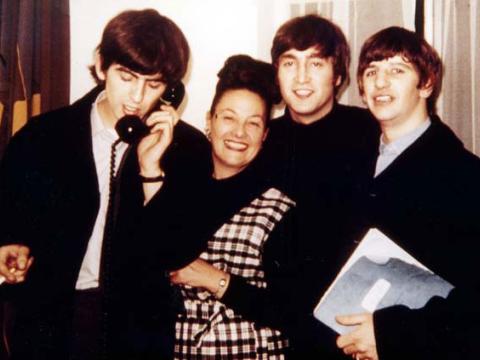 Binny Lum stands between George Harrison on a telephone, John Lennon and Ringo Starr.