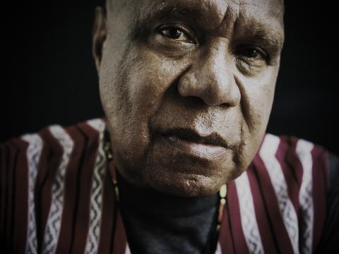 Close up of Archie Roach looking directly at camera, he is wearing a striped shirt.