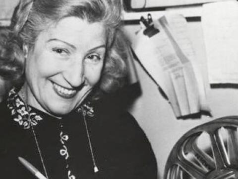 A woman smiling at the camera. There is a film reel in front of her. 