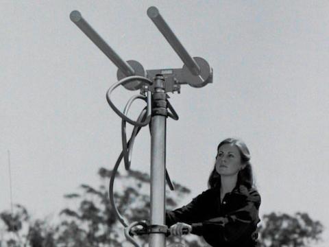 A woman is on the roof of a news cruiser van. She is operating a large metal technical instrument.