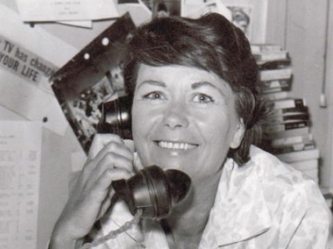 A woman with a telephone under her chin. She is smiling at the camera.