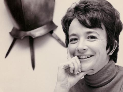 A woman smiles for the camera with her chin resting on her hand.