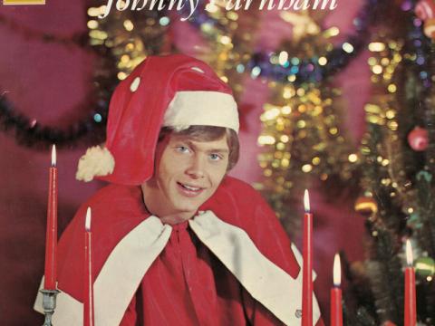 An album cover showing a young John Farnham dressed in a Santa outfit complete with hat. The text reads 'Christmas is ... Johnny Farnham'.
