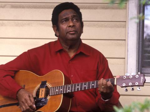 Jimmy Little wearing a red shirt playing guitar