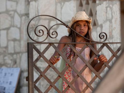 A young girl wearing a hat looking over an ron gate