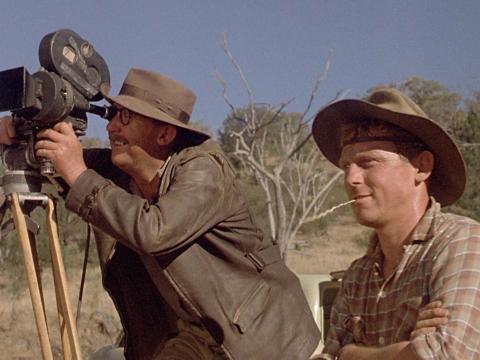 Bill Hunter looks through the viewfinder of a newsreel camera on location with his assistant, played by Chris Haywood, in the film Newsfront.