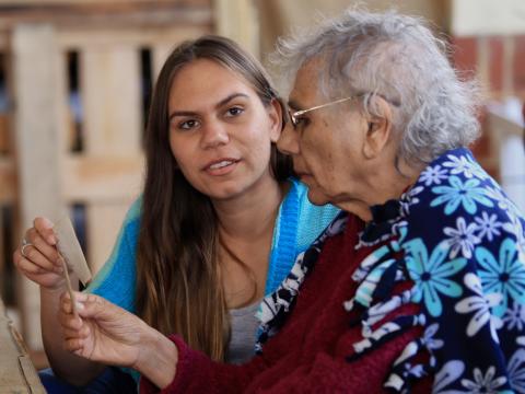 A young and elder woman are sitting at a table holding and looking at a photograph