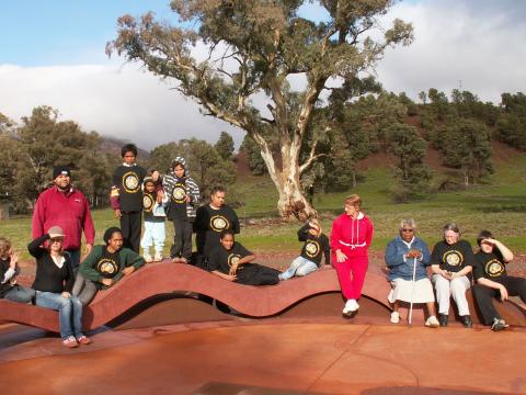 Group of people sitting on a wavy bench in a park.