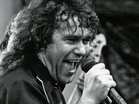 Close up of Jimmy Barnes singing into a microphone on stage. 