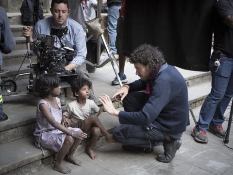 Lion director Garth Davis talking to Sunny Pawar (Young Saroo) and Rita Boy (Amita), who are sitting on a step with cinematographer Greig Fraser setting up a shot behind them