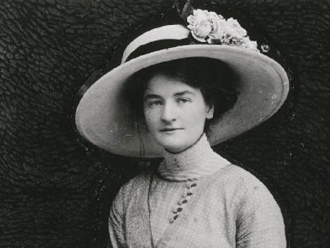 Portrait photo of Ella Caspers seated with handbag, gloves and large hat with flowers.