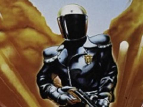 Black clad figure with bike helmet holding a gun.
