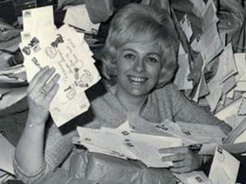 A woman smiling at the camera as she holds up lots of letters.